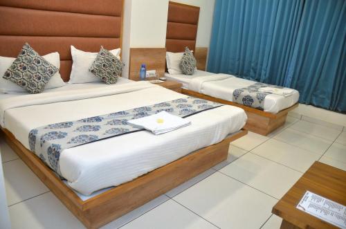 two beds in a hotel room with blue curtains at Hotel Neelkamal in Anand