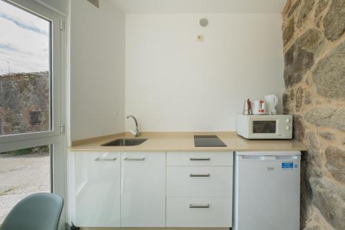 Cabaña de Nemiña (A casa de Anxo e Samu) في موتشيا: مطبخ مع دواليب بيضاء وميكرويف