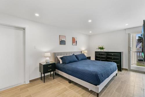 a white bedroom with a blue bed and a window at Fully Renovated Condo Steps from the Beach with Ocean View Balcony in South Padre Island