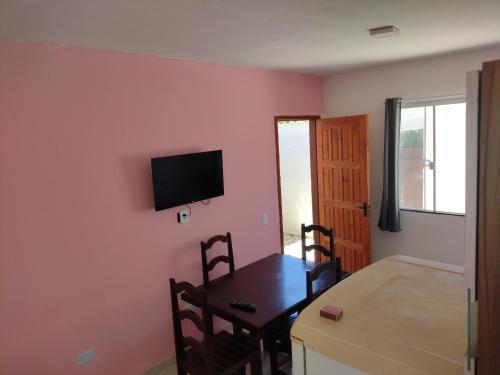 ein Esszimmer mit einem Tisch und einem TV an einer rosa Wand in der Unterkunft Casa enteira con piscina compartilhada in Búzios