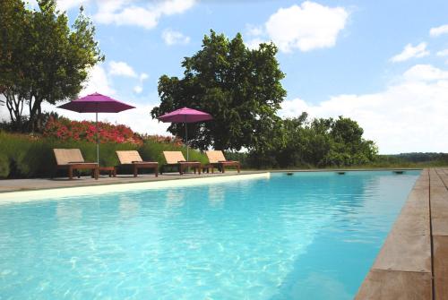 une piscine avec chaises et parasols dans une cour dans l'établissement La Maison de Bazugues, à Bazugues
