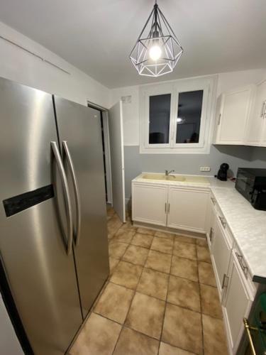 La cuisine est équipée d'un réfrigérateur en acier inoxydable et de placards blancs. dans l'établissement Grand appartement 3 chambres, à Perpignan