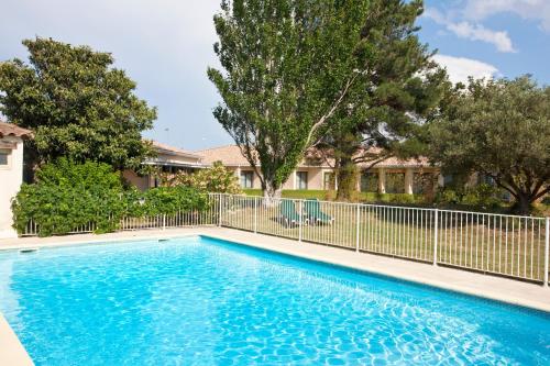 uma piscina com cerca e árvores em Hôtel Paradou Avignon Sud em Avignon