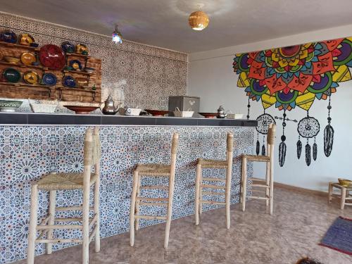 a kitchen with a counter with three stools in front at Happy Surf Hostel in Taghazout
