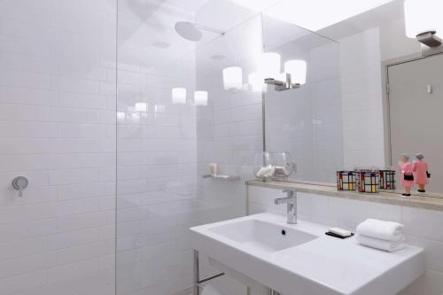 Baño blanco con lavabo y espejo en QT Canberra en Canberra