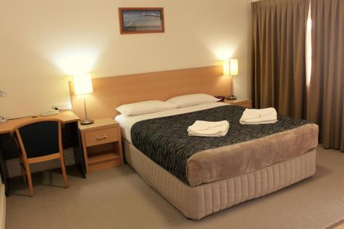 
a hotel room with a bed, chair, and nightstand at Rockhampton Palms Motor Inn in Rockhampton

