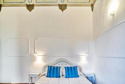 a white bedroom with a bed with blue pillows at Palazzo del Magnifico B&B in Siena