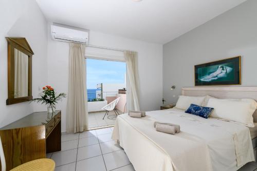 a white bedroom with a bed and a balcony at Bellevue Suites in Agios Nikolaos