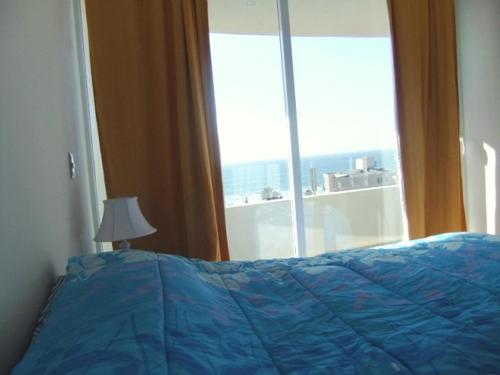 - un lit avec une couette bleue devant une fenêtre dans l'établissement Serena Holiday Vista, à La Serena