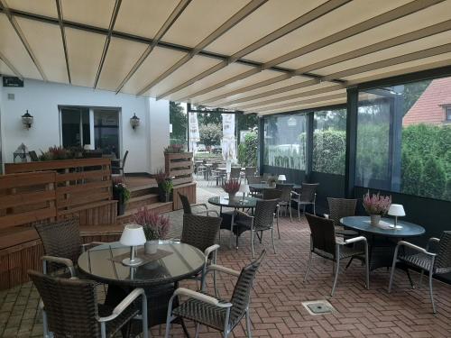 eine Terrasse mit Tischen, Stühlen und Fenstern in der Unterkunft Hotel Restaurant Zum Wacholderhain in Haselünne
