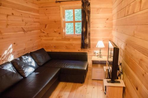 a living room with a black leather couch in a log cabin at Le Chalet De Louyère in Saint-Salvadour