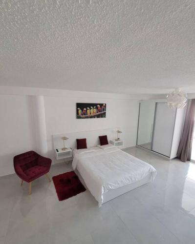 a white bedroom with a bed and a red chair at Hello Guyane, Suite Collection (5), 5 étoiles. in Cayenne