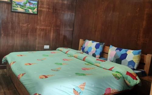 a bed with a green comforter and two pillows at Bluepine Cottages Pangot by Nature Nests in Nainital