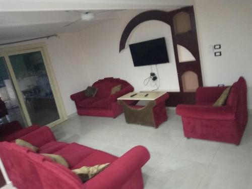 a living room with two red couches and a tv at قرية رمسيس الكيلو45 الساحل الشمالي in Borg El Arab