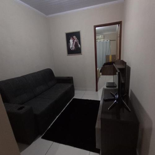a living room with a black couch and a mirror at Acomodação barata. in Campos dos Goytacazes