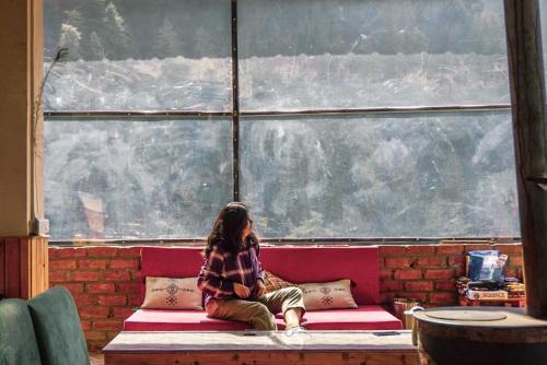 a person sitting on a bench in front of a window at ThePahadians Food & Stay in Jibhi