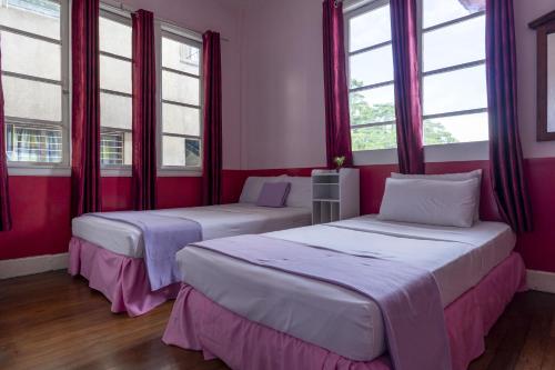 two beds in a room with red walls and windows at Old Orangewood Bed & Breakfast in Baguio