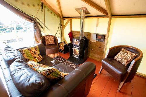 a living room with a leather couch and a stove at Hakuna Matata Safari Lodge - Sublime, off-grid digital detox with hot tub in Shelsley Walsh