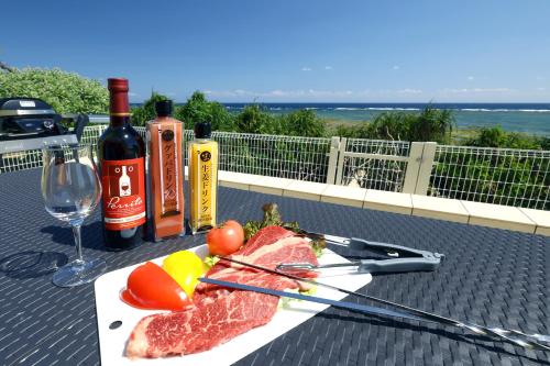 ein Teller Fleisch und Gemüse auf einem Tisch mit Weinflaschen in der Unterkunft オーシャンヴィラ徳之島-Ocean Villa Tokunoshima- in Tokunoshima