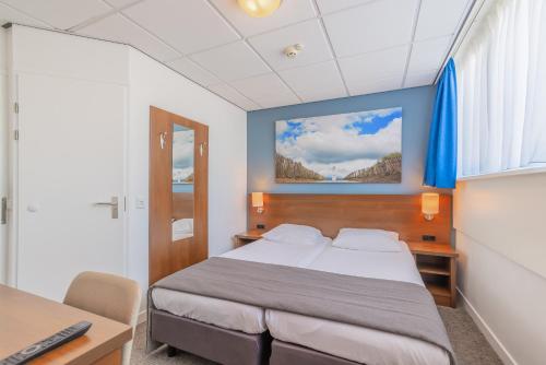a bedroom with a bed and a desk and a window at Hotel De Koningshof in Noordwijk aan Zee