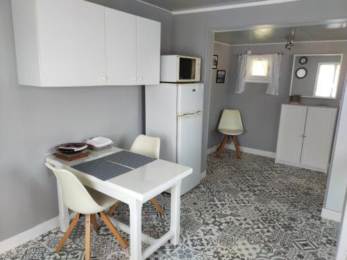 La cuisine est équipée d'une table et de chaises blanches ainsi que d'un réfrigérateur. dans l'établissement La ptite maison, à Rouxmesnil-Bouteilles