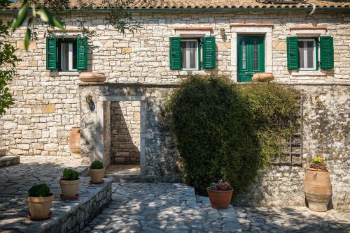 ein Steingebäude mit grünen Fenstern und Topfpflanzen in der Unterkunft Villa Eleni in Gaios