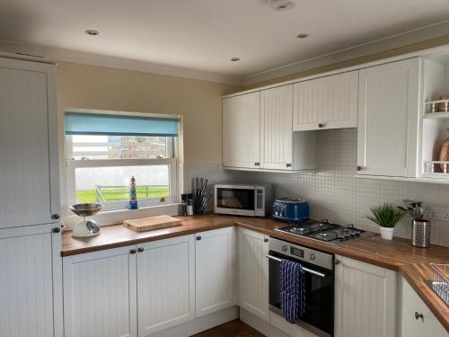 a kitchen with white cabinets and a stove top oven at Extended Fishermans cottage with stunning sea views in The Mumbles