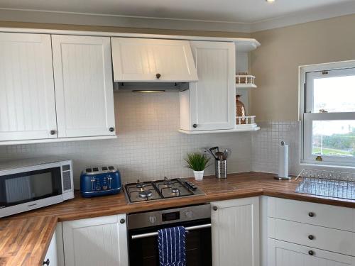 a kitchen with white cabinets and a stove and a microwave at Extended Fishermans cottage with stunning sea views in The Mumbles