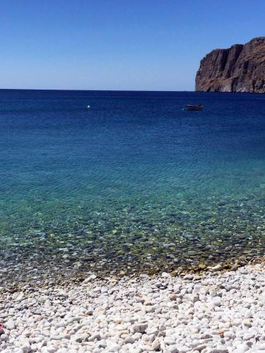 a rocky beach with the ocean and a boat in the water at Akroyiali Apartments in Gerolimenas