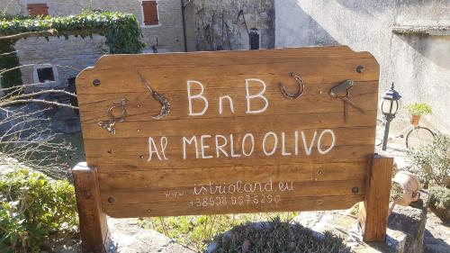a sign on a wooden post in front of a stone wall at B&B al Merlo Olivo in Buje