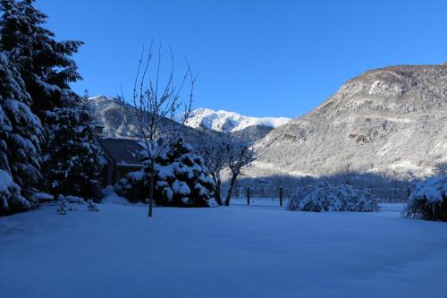 a snow covered field with a house and mountains at Villa Art Natura in Juzet-de-Luchon