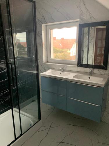 La salle de bains est pourvue d'un lavabo bleu et d'une fenêtre. dans l'établissement Bialy domek, à Rowy