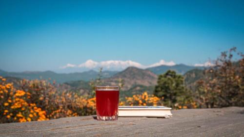 a glass of red liquid sitting on a table with a book at Itmenaan Estate in the Himalayas in Almora