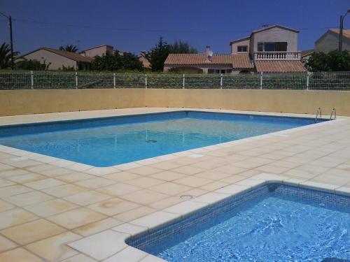 une grande piscine avec du carrelage et une maison dans l'établissement Location d'un pavillon de vacances, à Marseillan