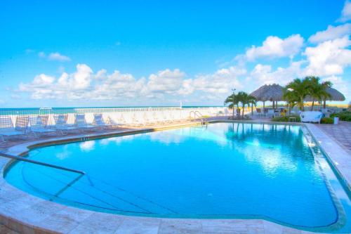 a large swimming pool with chairs and the ocean at 103 - Sandy Shores in St. Pete Beach