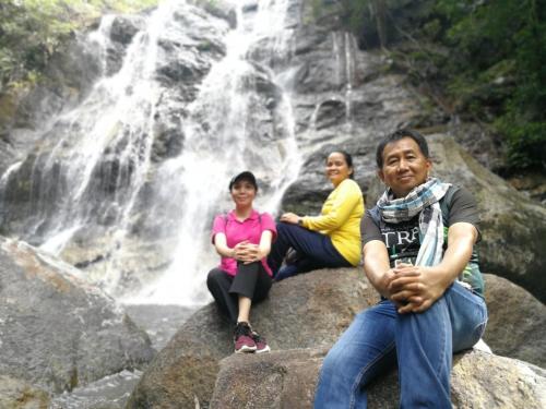 three people sitting on rocks in front of a waterfall at โฮมสเตย์บ้านนายสิงโตเขาคูหา in Ban Khu Ha Nai (1)