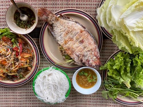 a table topped with plates of food and vegetables at โฮมสเตย์บ้านนายสิงโตเขาคูหา in Ban Khu Ha Nai (1)