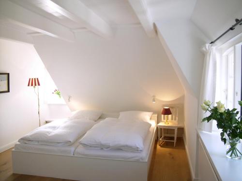 ein weißes Bett in einem weißen Zimmer mit Fenster in der Unterkunft Weidemannhaus Wohnung 6 "Galerie" in Keitum