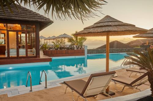 a swimming pool with two chairs and an umbrella at Secrets Lanzarote Resort & Spa - Adults Only (+18) in Puerto Calero