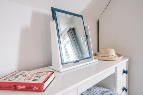 a mirror and a book on a white shelf at Rest Ashored, Aldeburgh in Aldeburgh