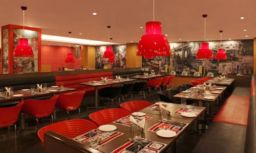 ニューデリーにあるレッド フォックス ホテル デリー エアポートのテーブルと椅子、赤いシャンデリアのあるレストラン