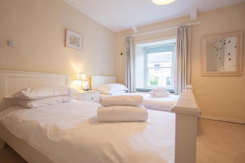 een slaapkamer met twee bedden met witte lakens en een raam bij Gargoyle Cottage in St. Agnes 