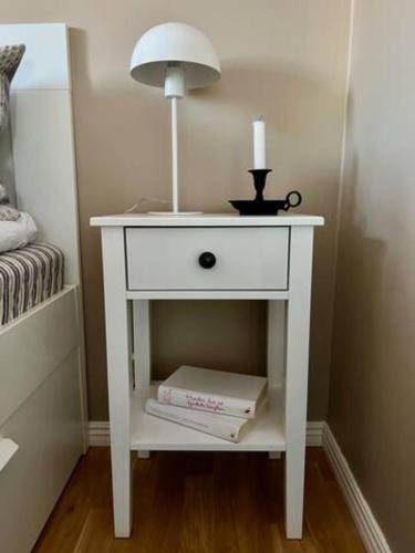 a white bedside table with a lamp and a book at The Novac's Cottage in Råneå