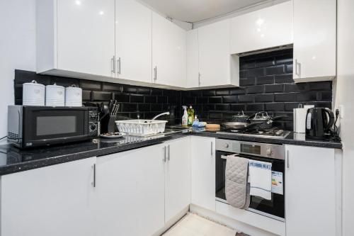 a kitchen with white cabinets and a microwave at Charming 1-Bed Basement Apartment in Lewisham in London