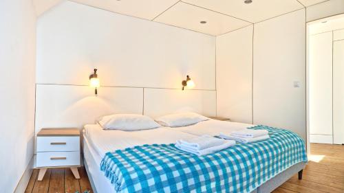 a white bedroom with a bed with a blue checked blanket at Domy na Wodzie na Mazurach in Pisz