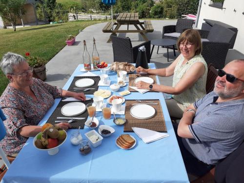 two women and a man sitting at a blue table with food at B&B Au fil des saisons sur la Wiels in Fauvillers