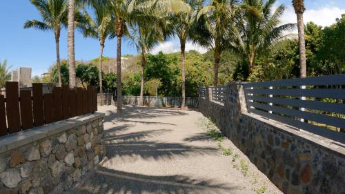 a stone wall with palm trees and a fence at Ô Ruisseau Lodges - Lodge Dattier in Saint-Louis