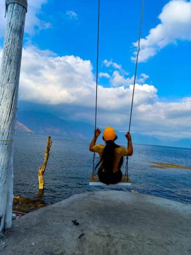 a person sitting on a swing over the water at Hotel Porto Bello in San Pedro La Laguna