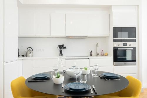 a white kitchen with a black table and yellow chairs at 3-bedroom apartment in the heart of Cannes in Cannes