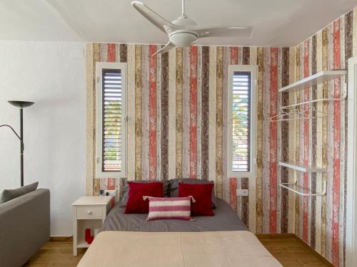 een slaapkamer met een bed met rode kussens en een plafondventilator bij Apartamento Retiro Sol in Denia